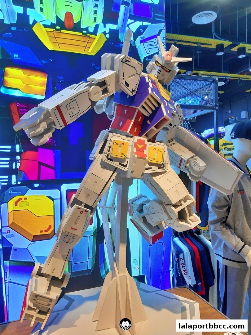 A large Gundam model stands prominently in a brightly lit shop, showcasing merchandise.