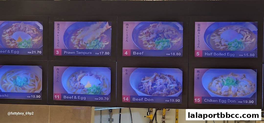 A digital menu board displaying various Japanese udon and donburi dishes with prices.