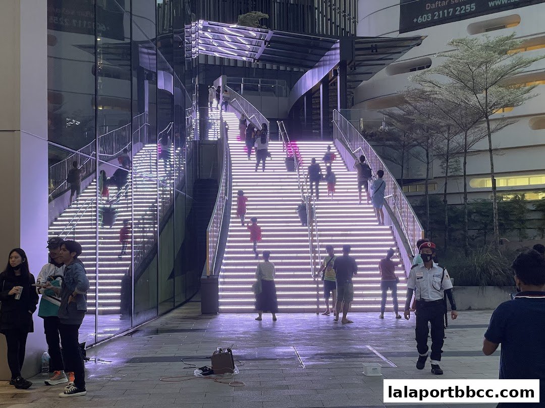 People ascend a brightly lit staircase at the Gate Plaza North entrance at night.