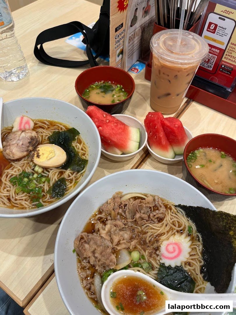 Two bowls of ramen, miso soup, watermelon slices, and a drink on a table.
