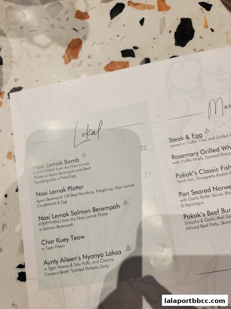 A close-up view of a menu from POKOK LaLaport, showcasing various Malaysian dishes.