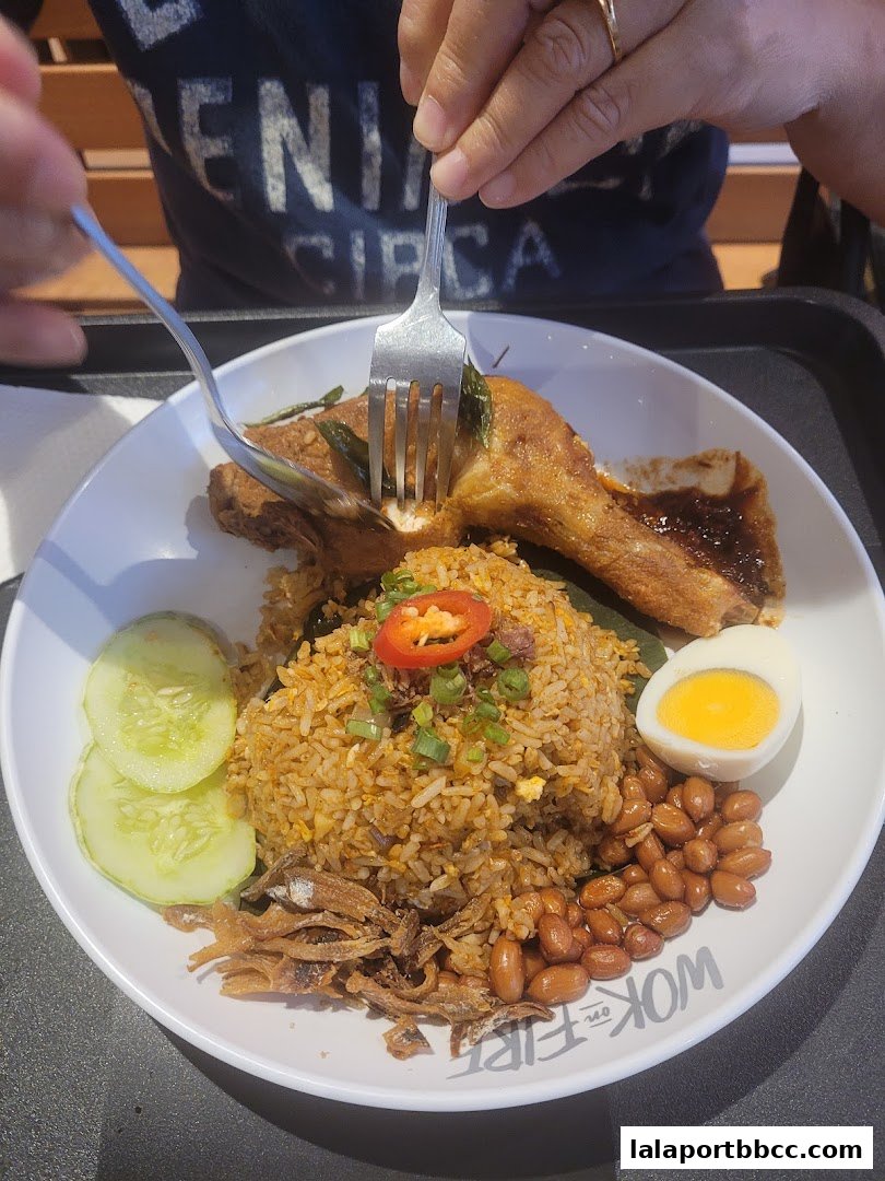 A person is eating a plate of Nasi Lemak with fried chicken and a hard-boiled egg.
