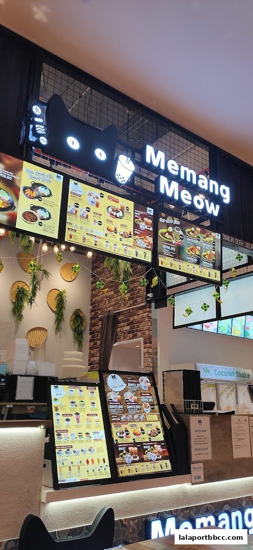 A brightly lit menu board displays various food and drink items with prices at Memang Meow.