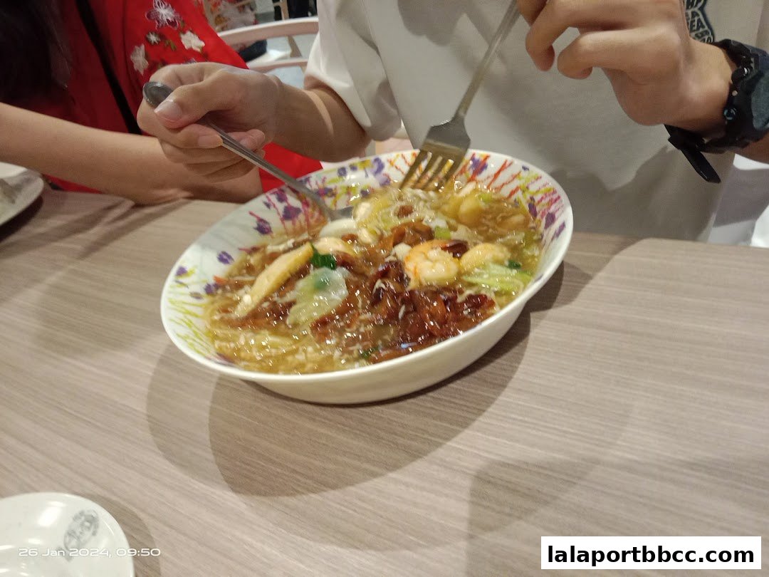 A close-up shot of a person eating a bowl of Hokkien Mee with shrimp and vegetables.