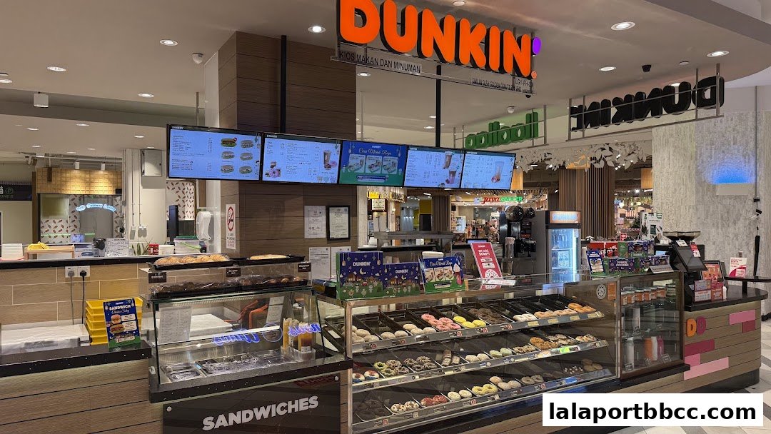 A Dunkin' Donuts shop counter displaying a variety of donuts and sandwiches, with digital menus above.