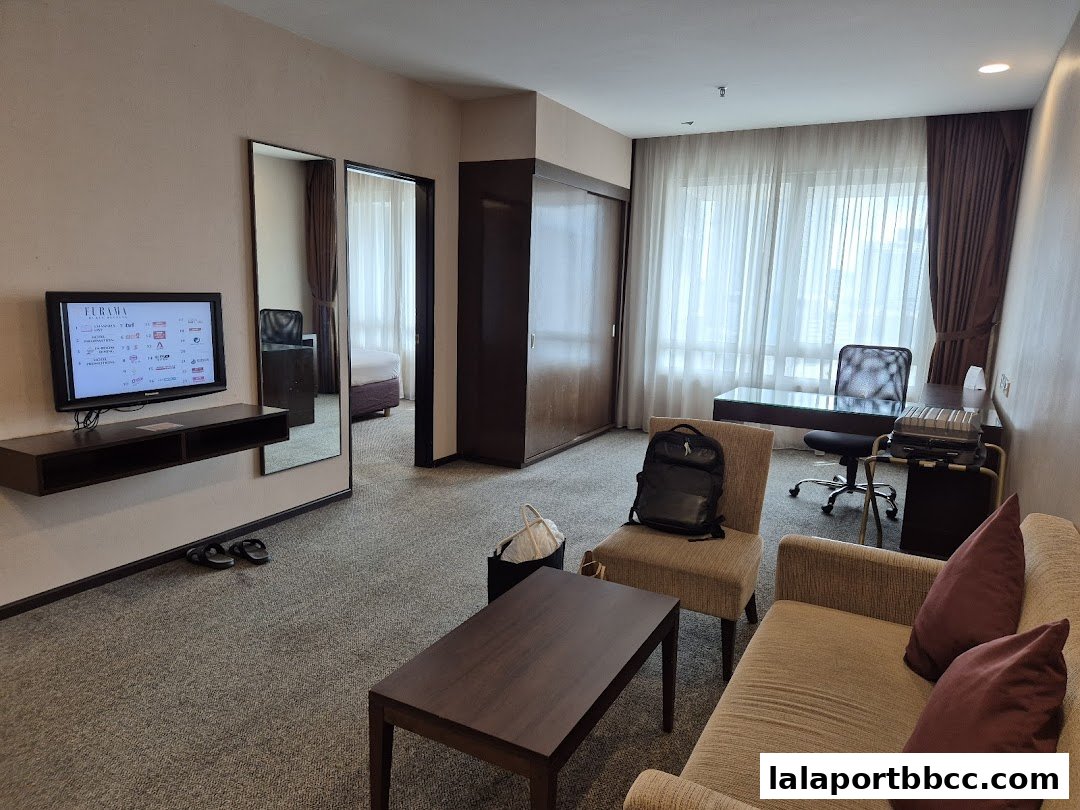 A hotel room interior featuring a sofa, desk, television, and a bed visible in a mirror.