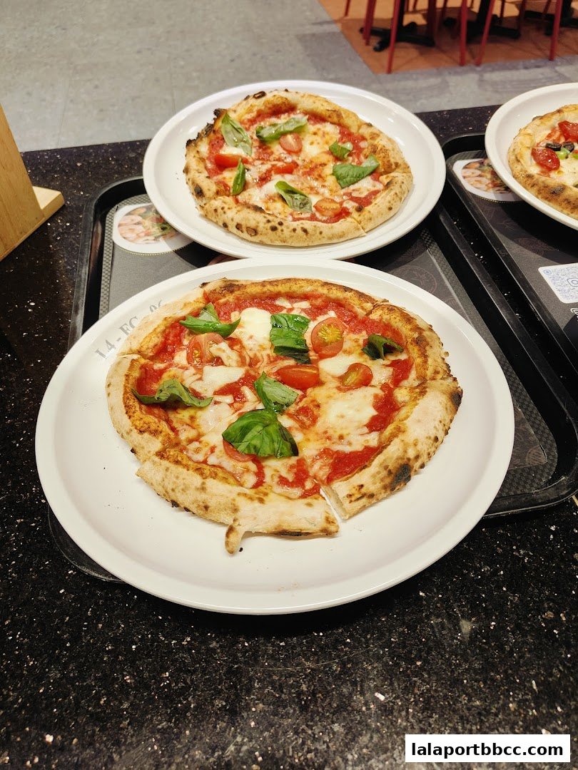 Two delicious pizzas with fresh basil and tomatoes on white plates.