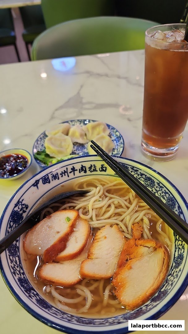 A bowl of noodle soup with sliced meat, dumplings, and a glass of iced tea.