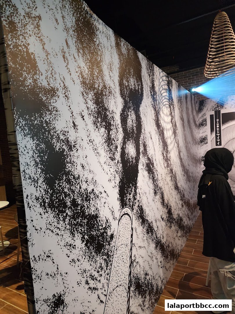 A person stands near a large black and white mural with a projected light beam.