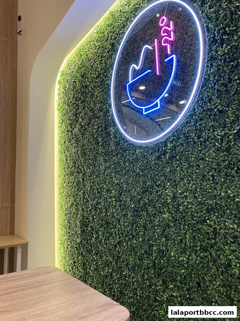 A neon sign with a bowl and steam above a green wall with a wooden table.