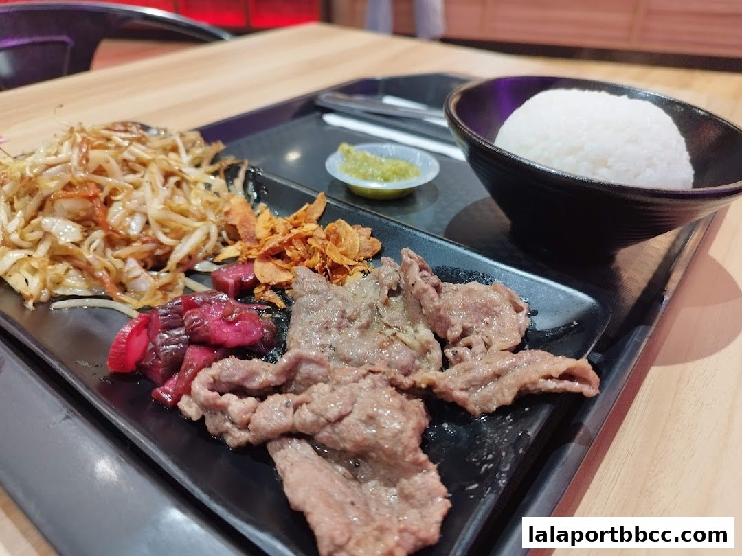 A close-up of a teppanyaki meal with grilled meat, stir-fried vegetables, rice, and a dipping sauce.