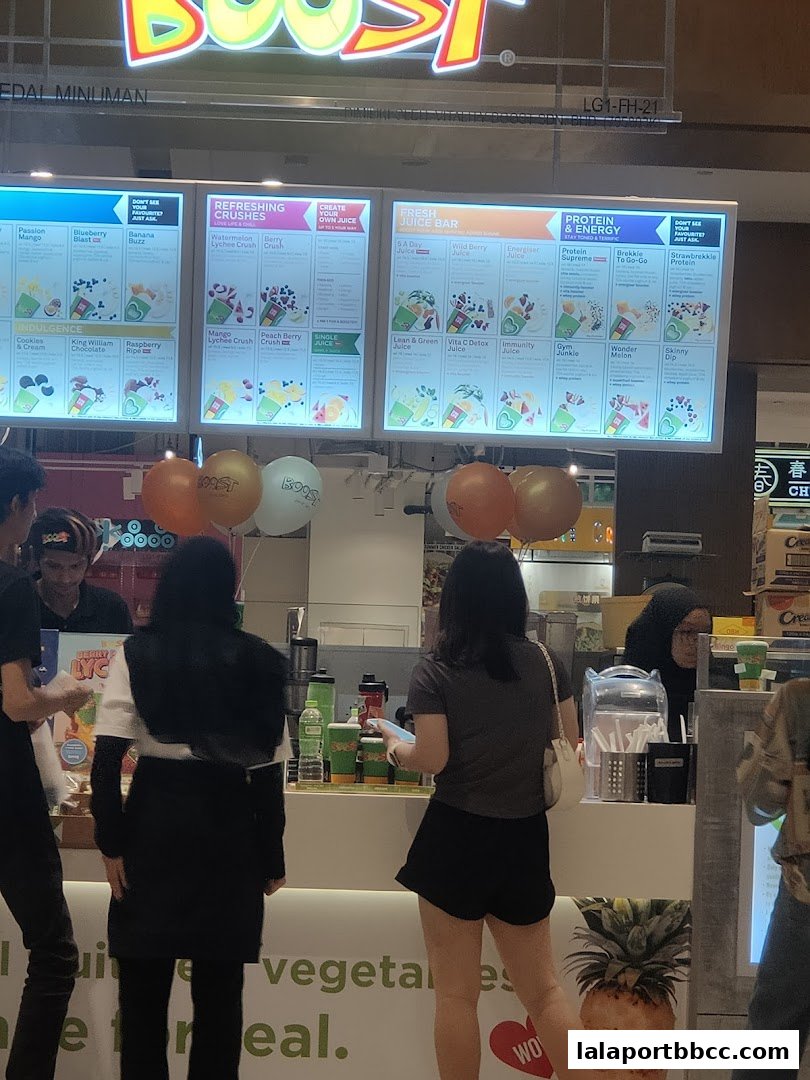 A Boost Juice counter with illuminated menus displaying various drinks and customers ordering.