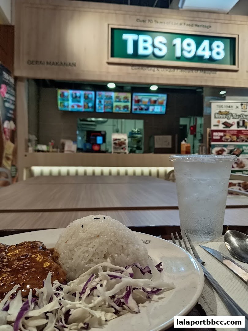 A plate of rice with meat and salad, next to a drink at TBS 1948.