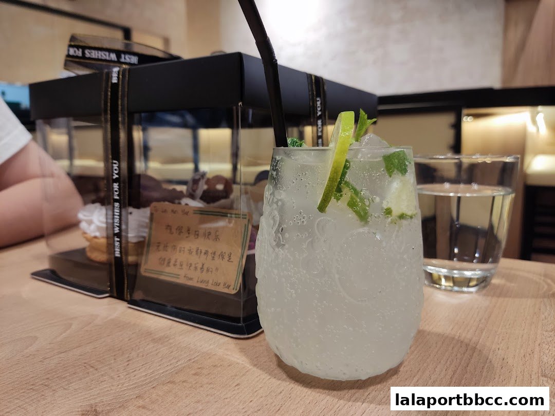 A refreshing drink with lime and mint next to a box of cupcakes.