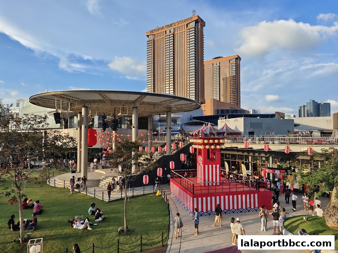 People enjoying a sunny day at a lively outdoor plaza with a stage and festive decorations.