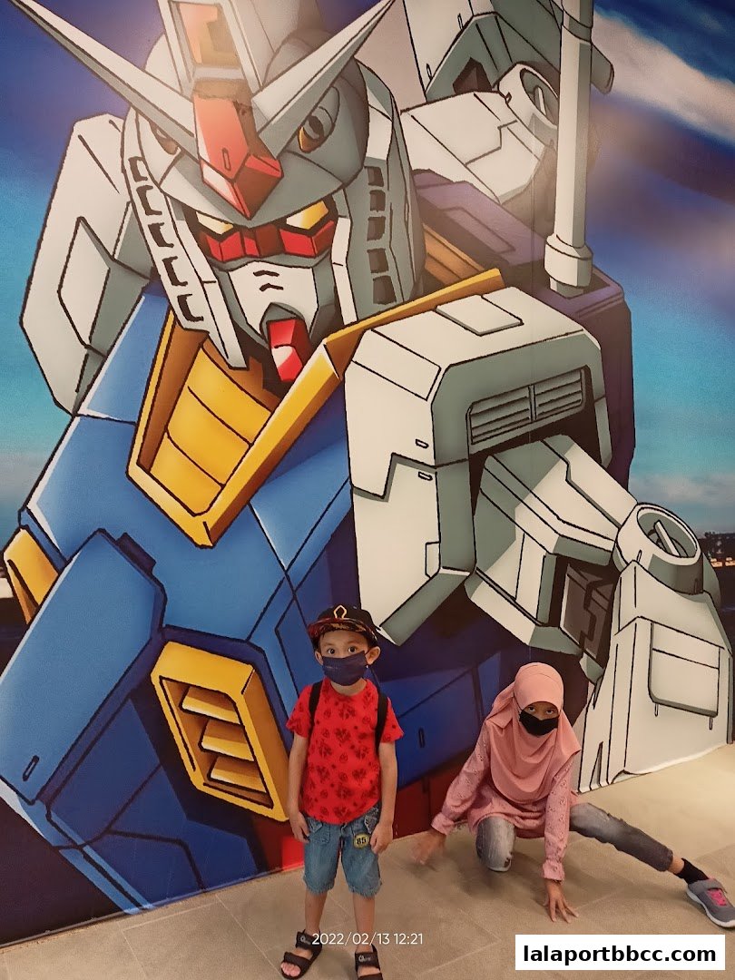 Two children pose in front of a large Gundam mural at MR.TOY Lalaport.