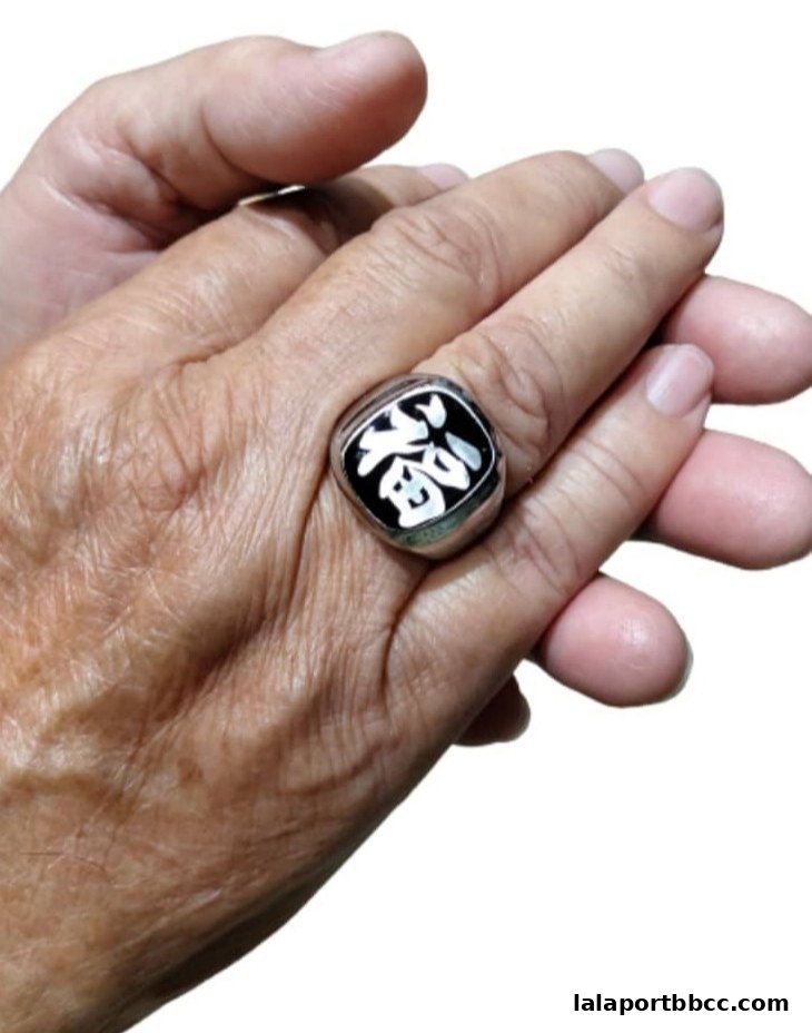 A hand wearing a silver ring with a black square face featuring a white Chinese character.