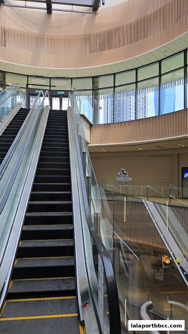Escalators and interior of a modern shopping mall with wooden accents and large windows.