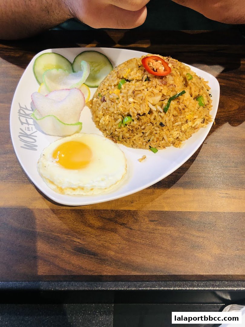 A plate of fried rice with a fried egg, cucumber slices, and crackers.