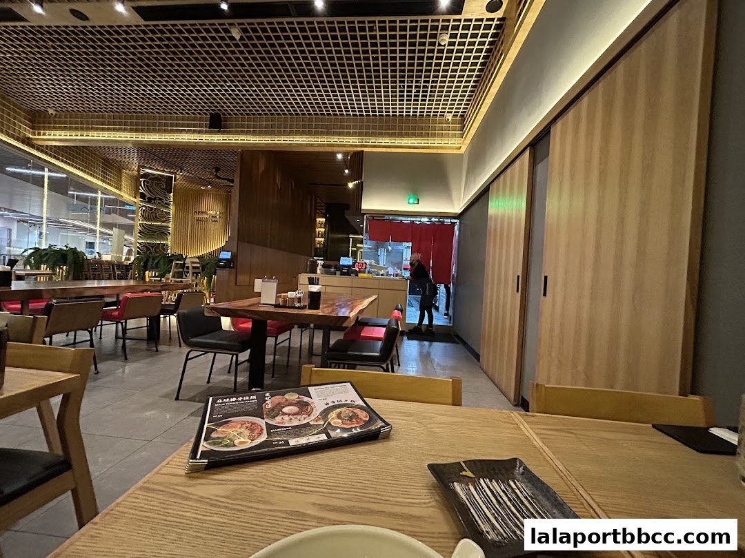 Interior of a modern Japanese restaurant with wooden tables and chairs, featuring a menu on a table.