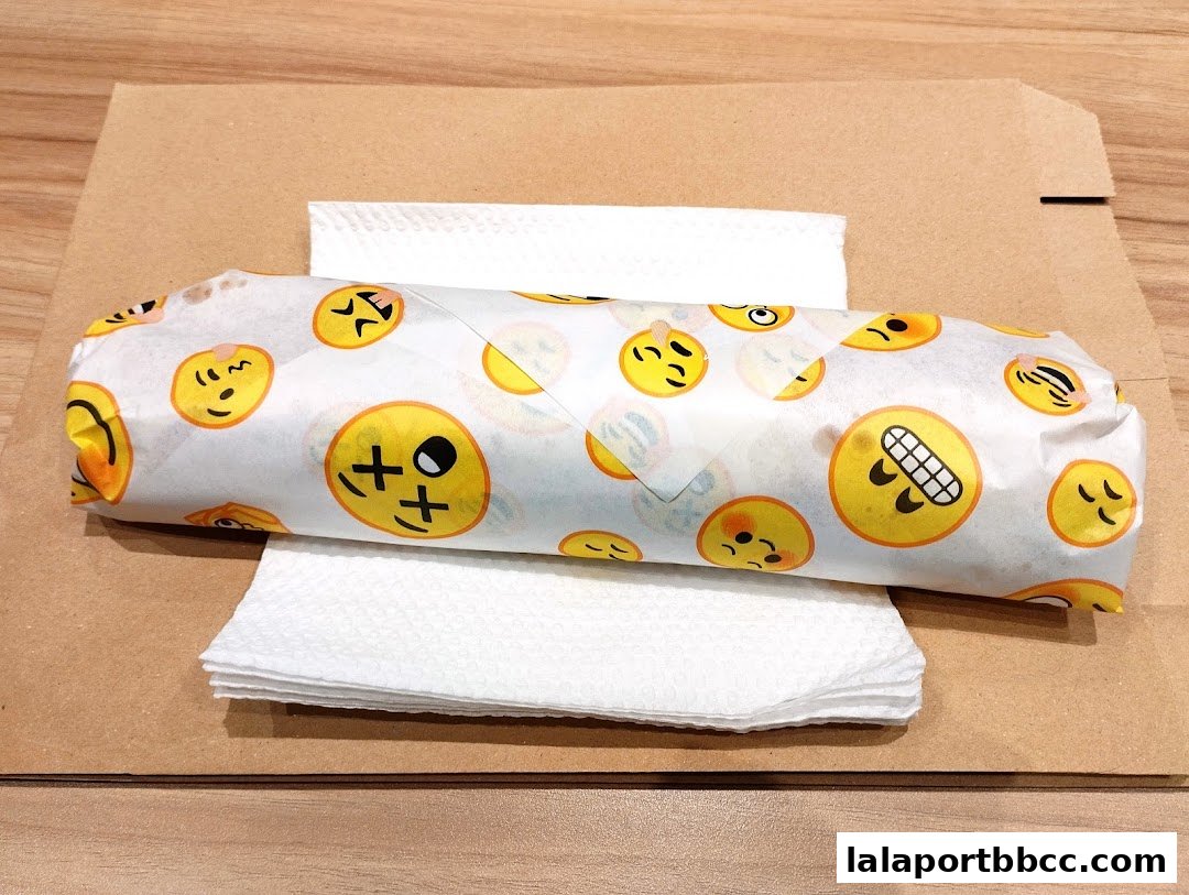A kebab wrapped in paper with various emoji designs, placed on napkins.