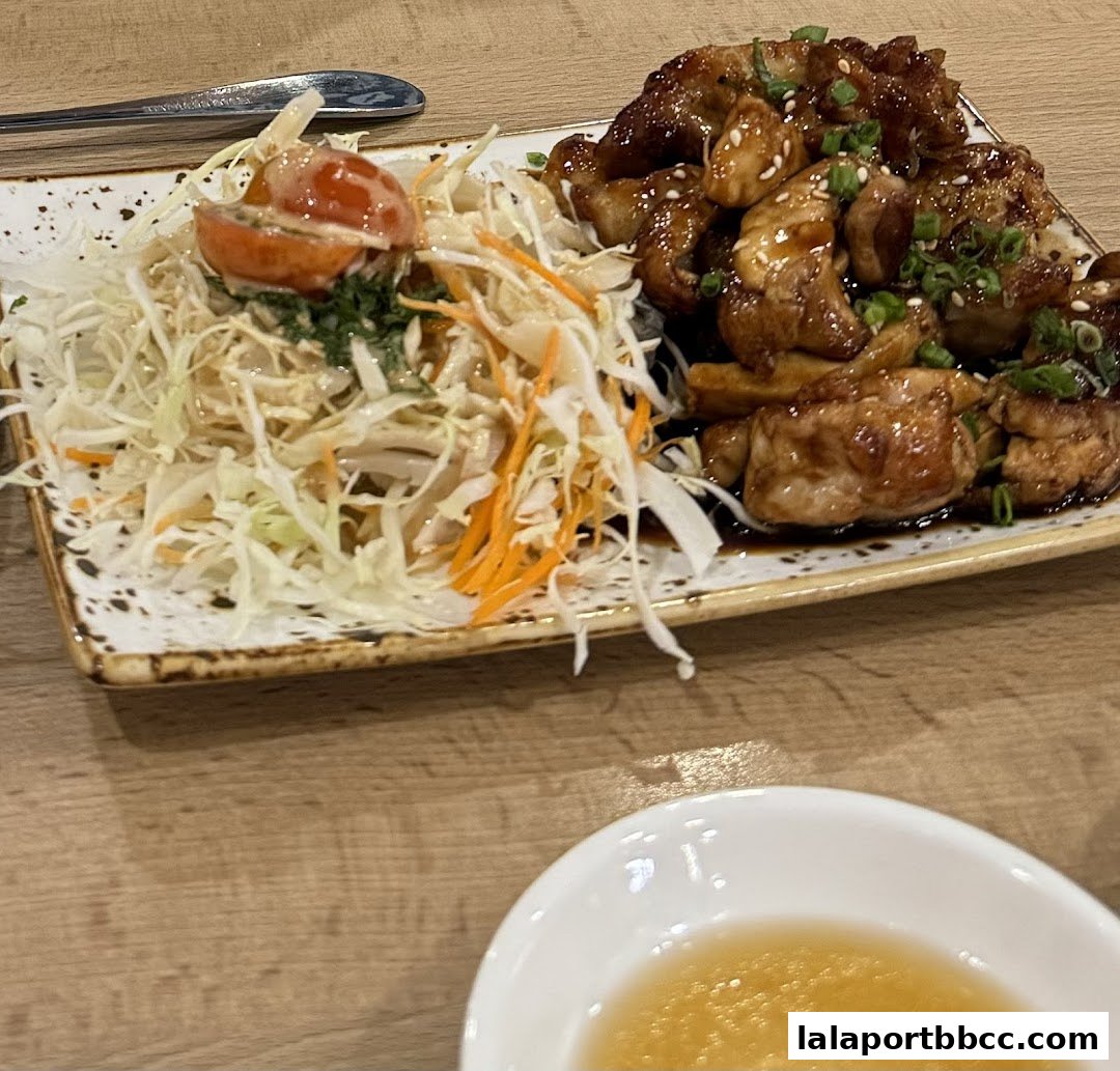 A plate of teriyaki chicken with a side salad and a dipping sauce.