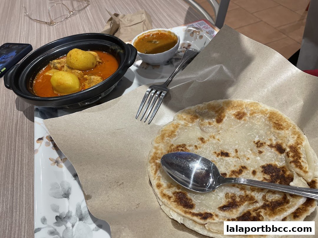 A close-up of a delicious Nasi Lemak meal with curry, potatoes, and roti canai.