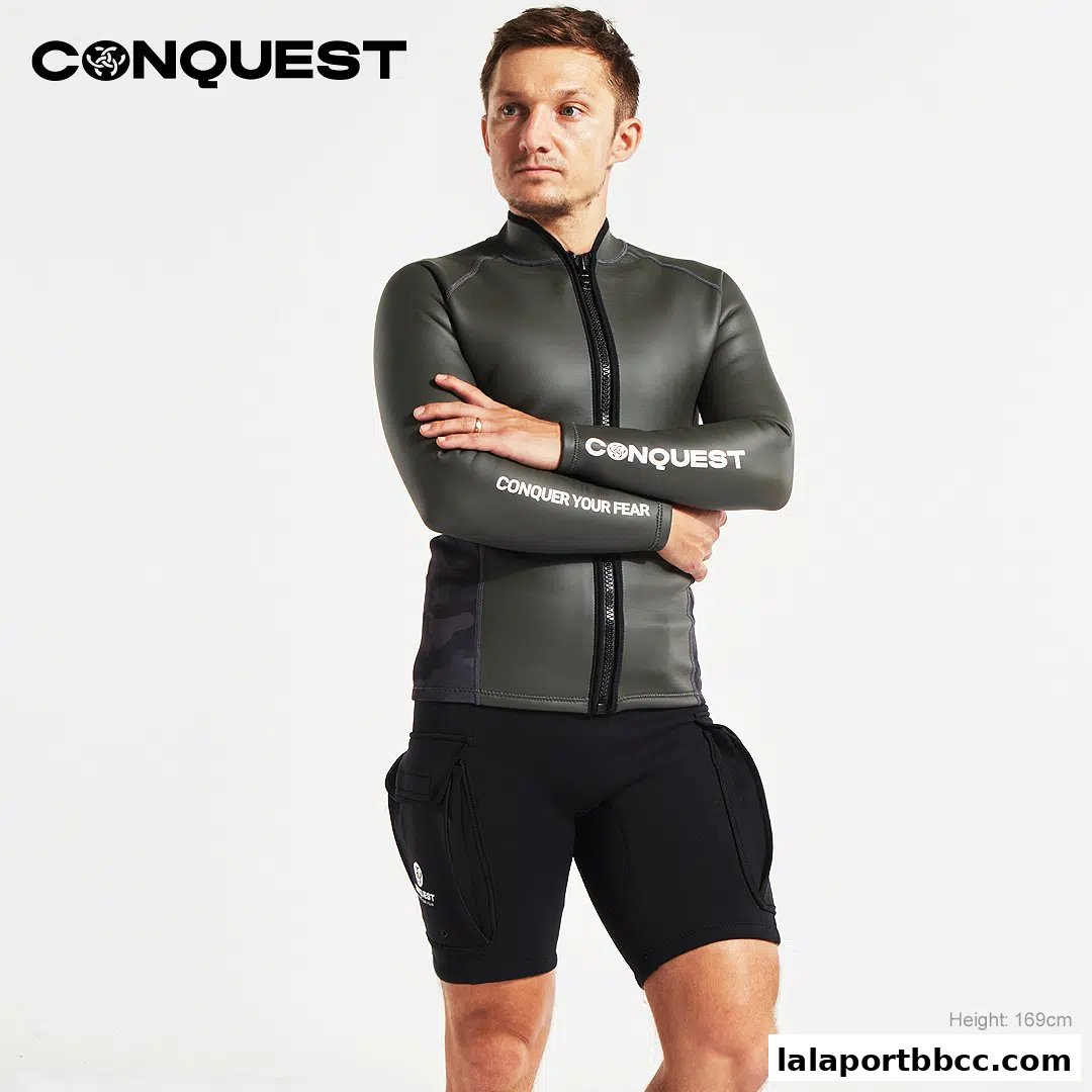 A man models a CONQUEST wetsuit jacket and shorts, with text on the sleeve.