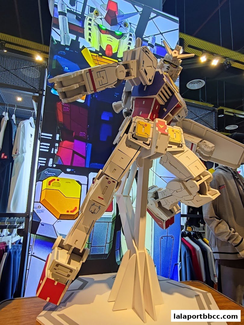 A large Gundam model displayed in a retail store with clothing racks in the background.