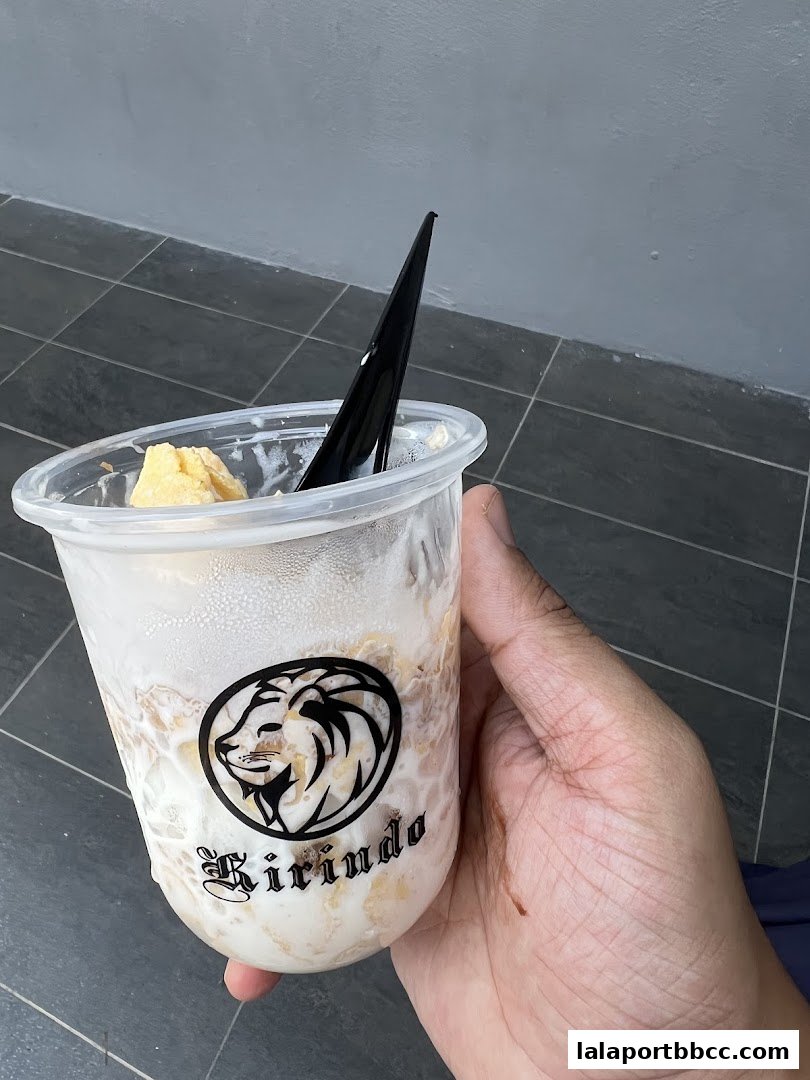 A hand holds a clear plastic cup with a dessert and a black spoon, featuring the Kirindo logo.