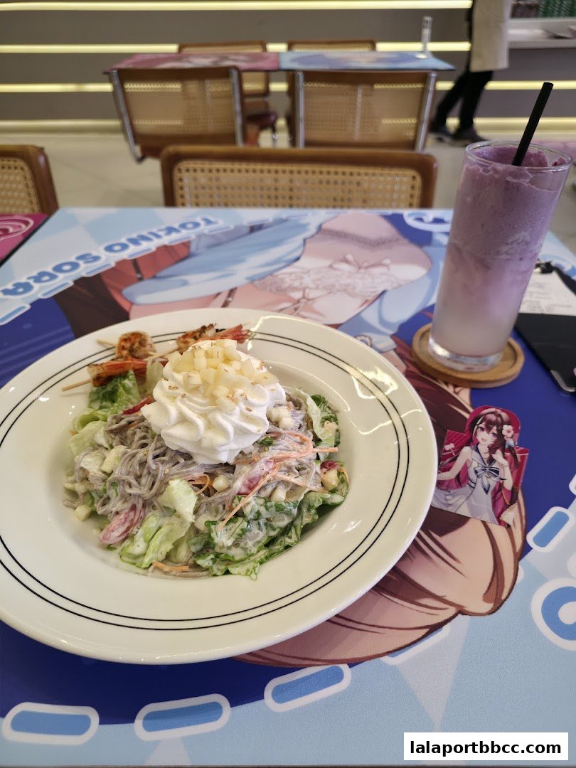 A salad and a purple drink are on a table with anime-themed decor.