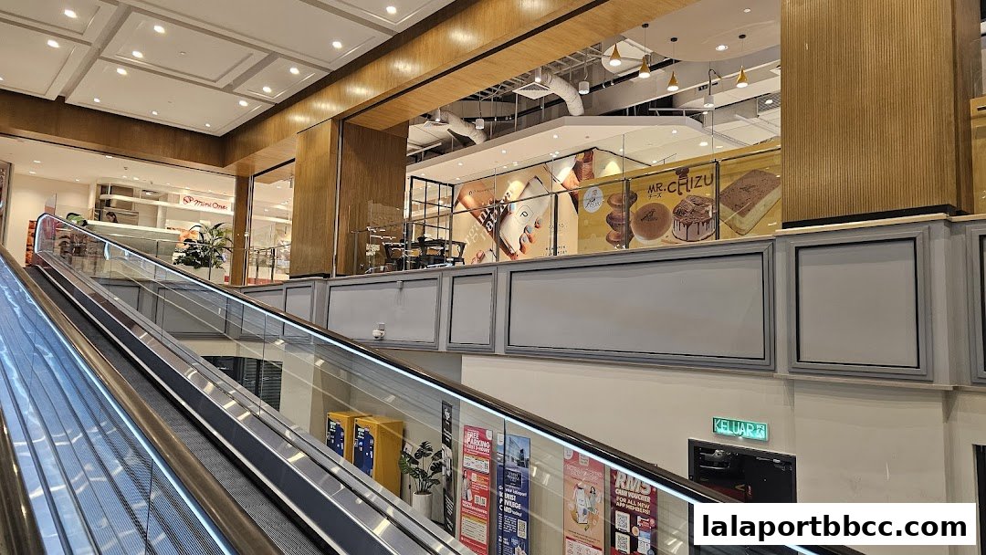 An escalator in a shopping mall leads to shops, including one with dessert displays.