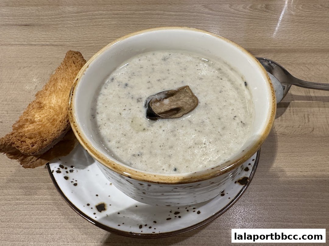A bowl of creamy mushroom soup with a slice of toasted bread and a spoon.