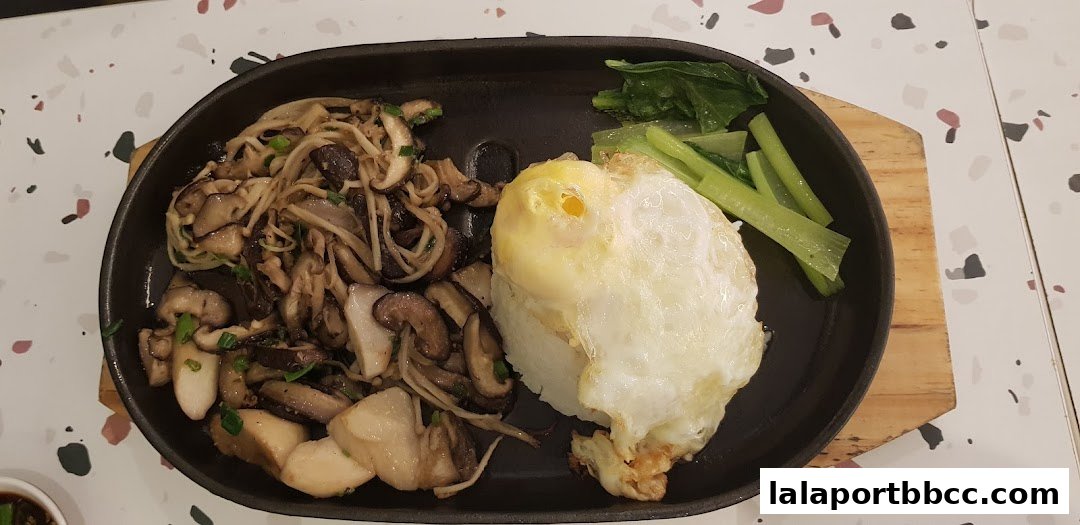 A sizzling claypot dish with mixed mushrooms, rice, a fried egg, and greens.