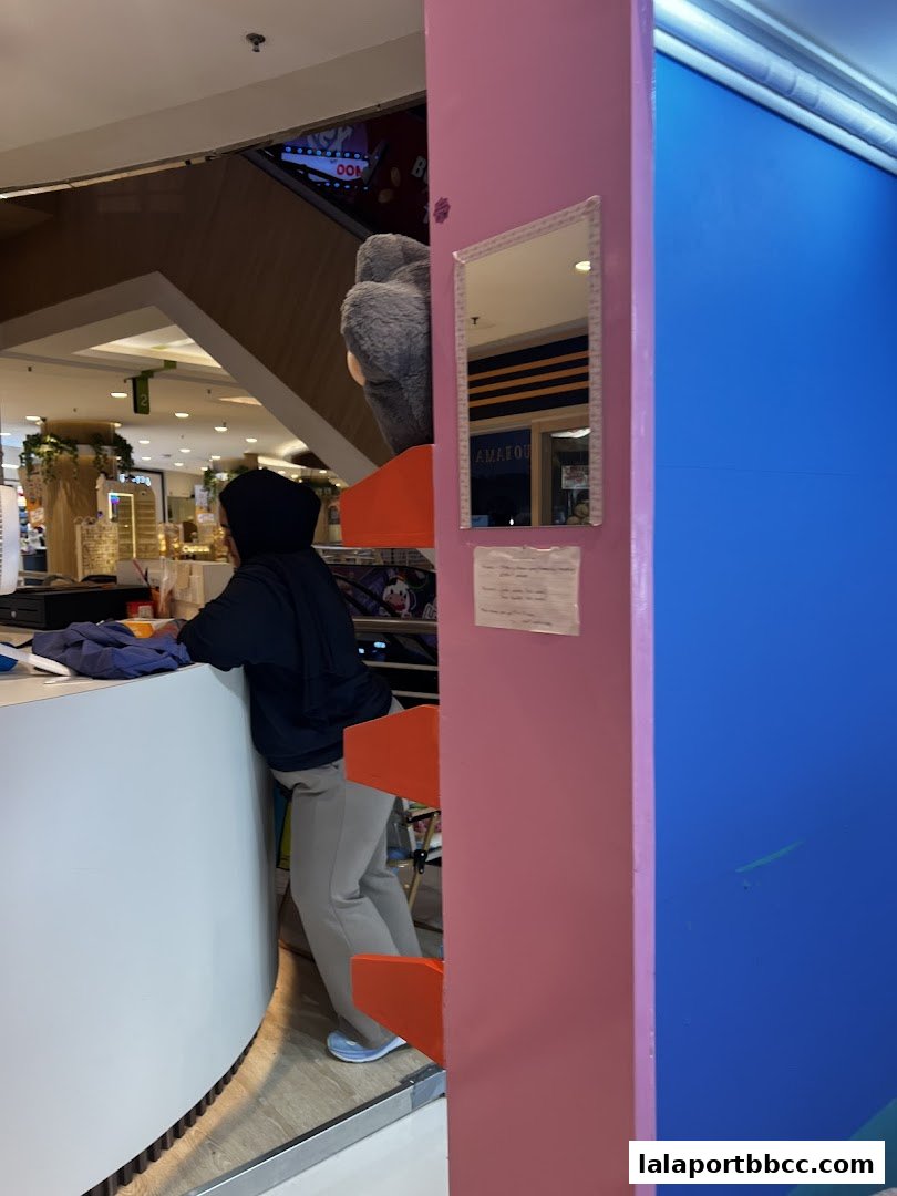 A person stands behind a counter in a brightly lit shop with a large stuffed animal.