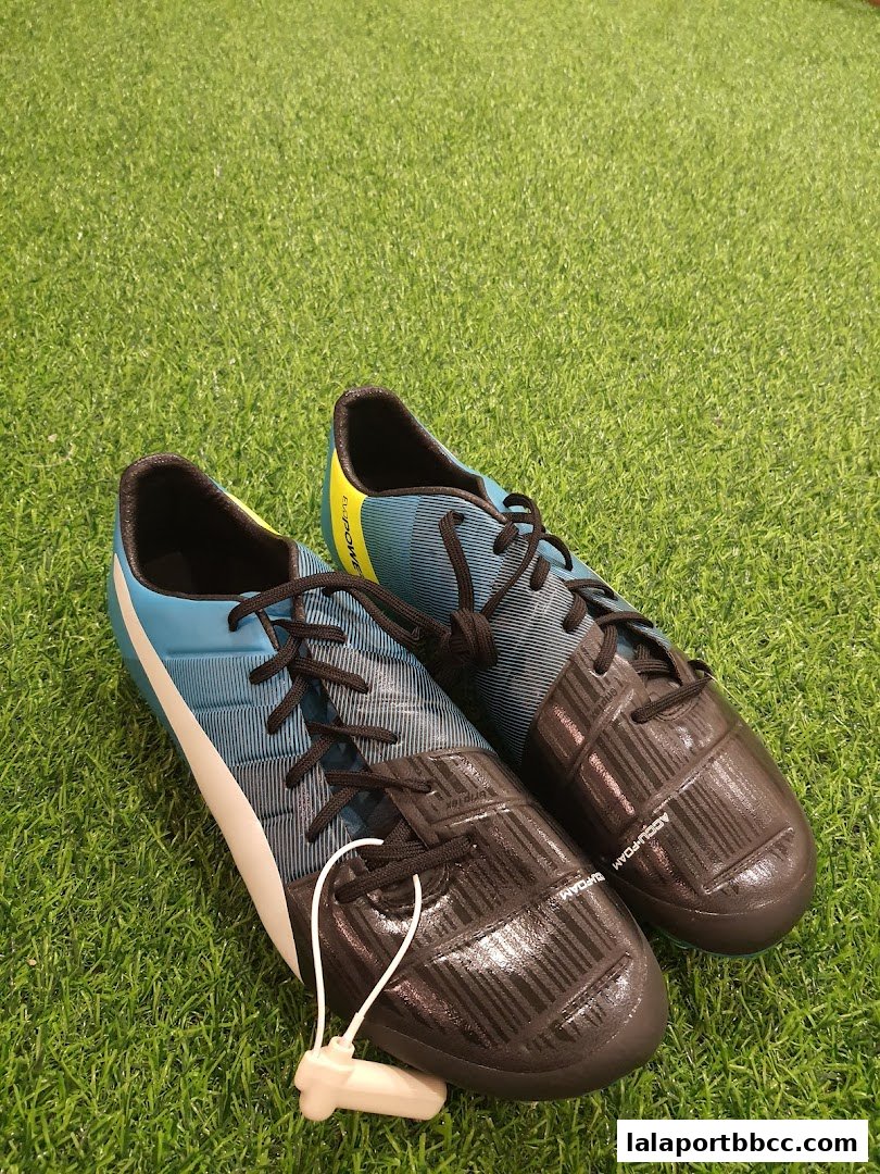 A pair of blue and black soccer cleats with a security tag on a grassy surface.