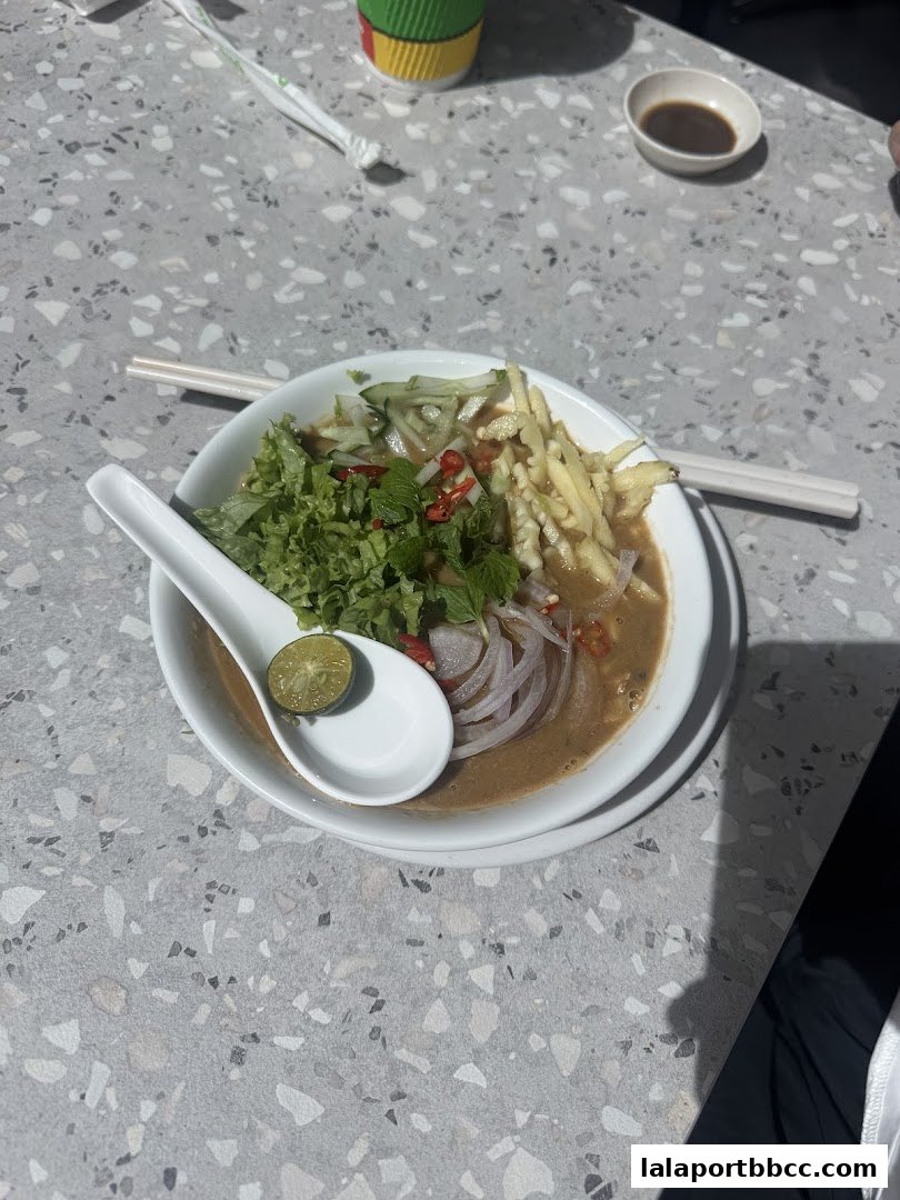 A bowl of Laksa with fresh toppings and a lime wedge, served with chopsticks.