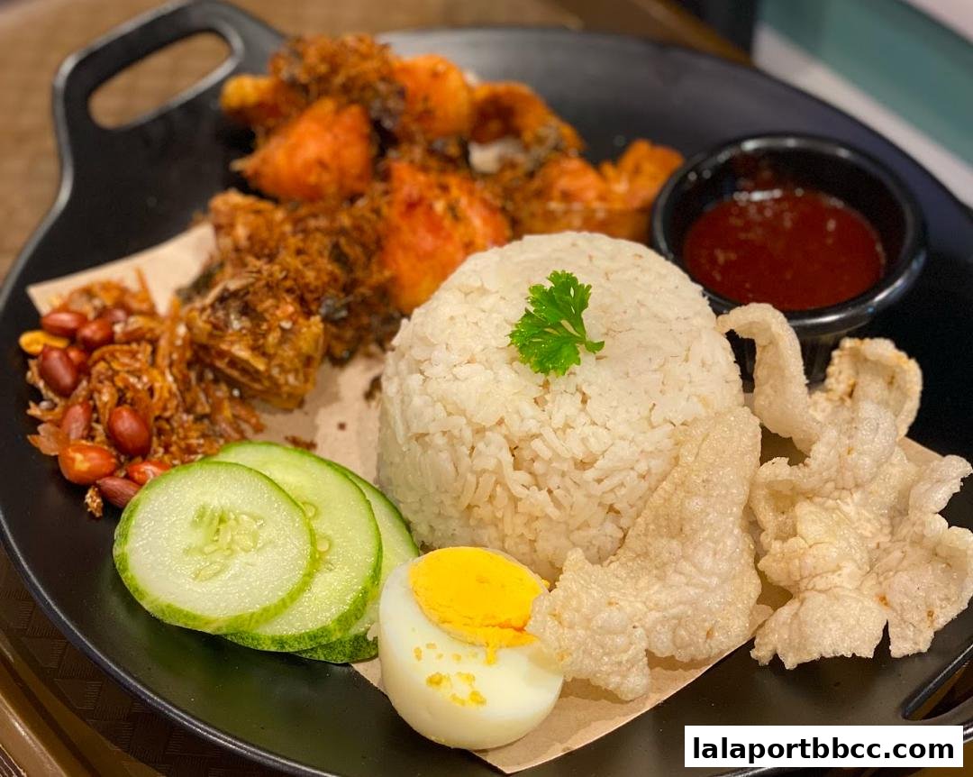 A delicious plate of Nasi Lemak with fried chicken, rice, egg, cucumber, and sambal.
