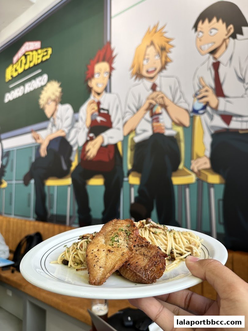 A plate of pasta with grilled fish is held up in front of a mural of anime characters.
