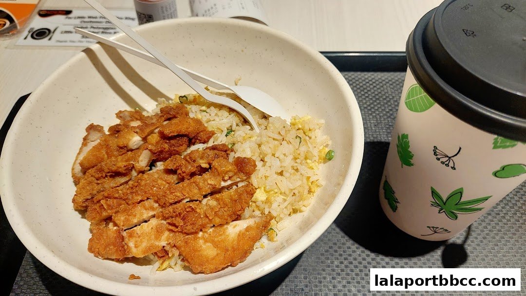A bowl of fried rice with crispy chicken and a beverage cup.