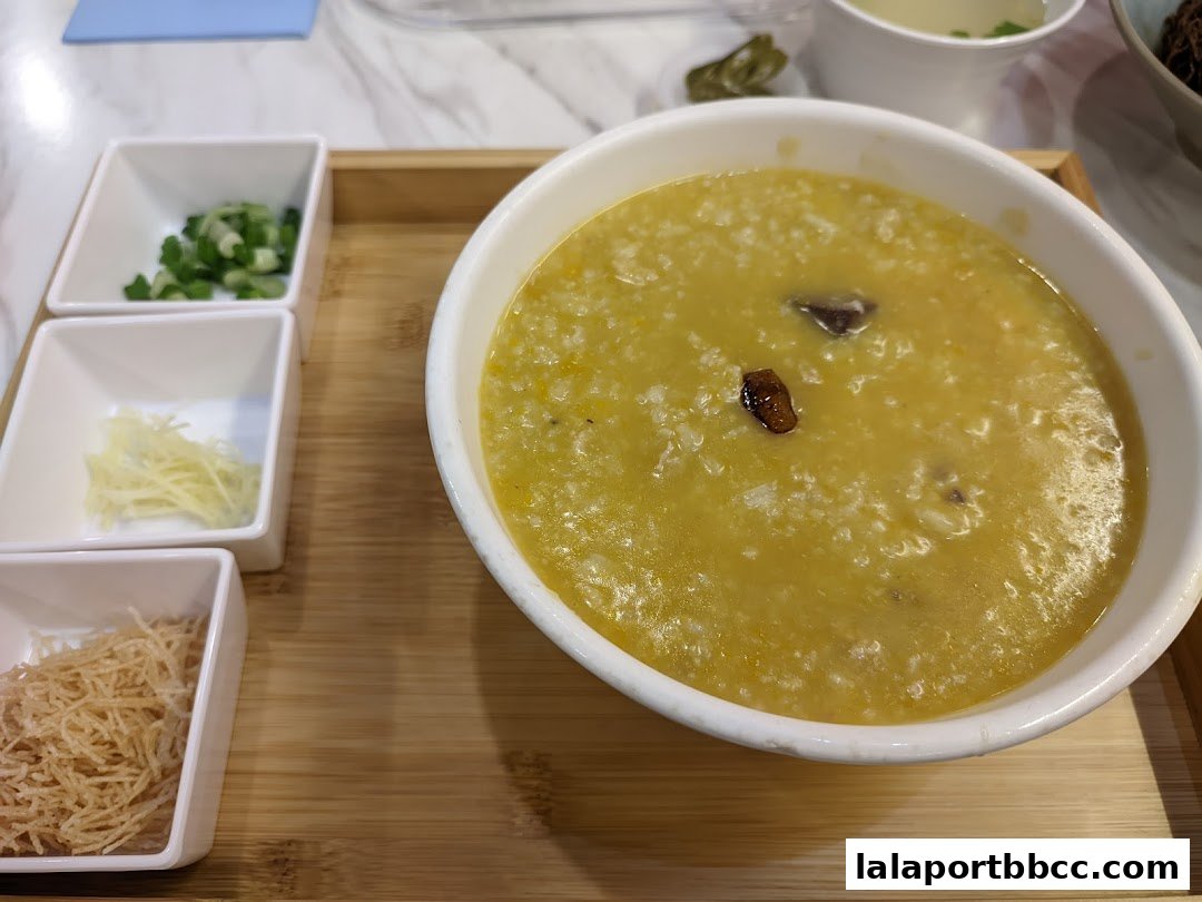 A bowl of congee with side dishes of chopped scallions, ginger, and crispy noodles.