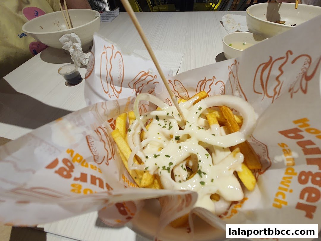 A close-up shot of french fries topped with mayonnaise and onion rings.