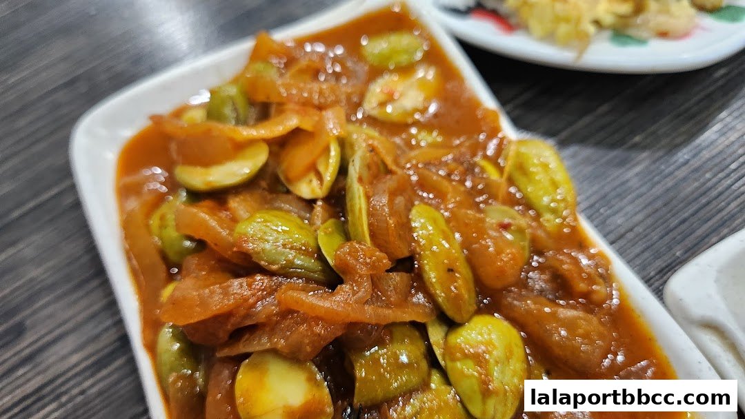 A close-up shot of a white plate filled with stir-fried petai beans in a savory sauce.