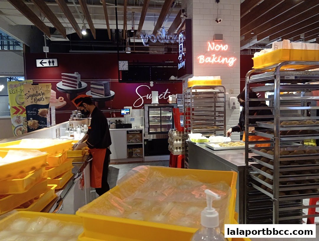 A baker works behind the counter at Rotiboy, with trays of buns and cakes visible.