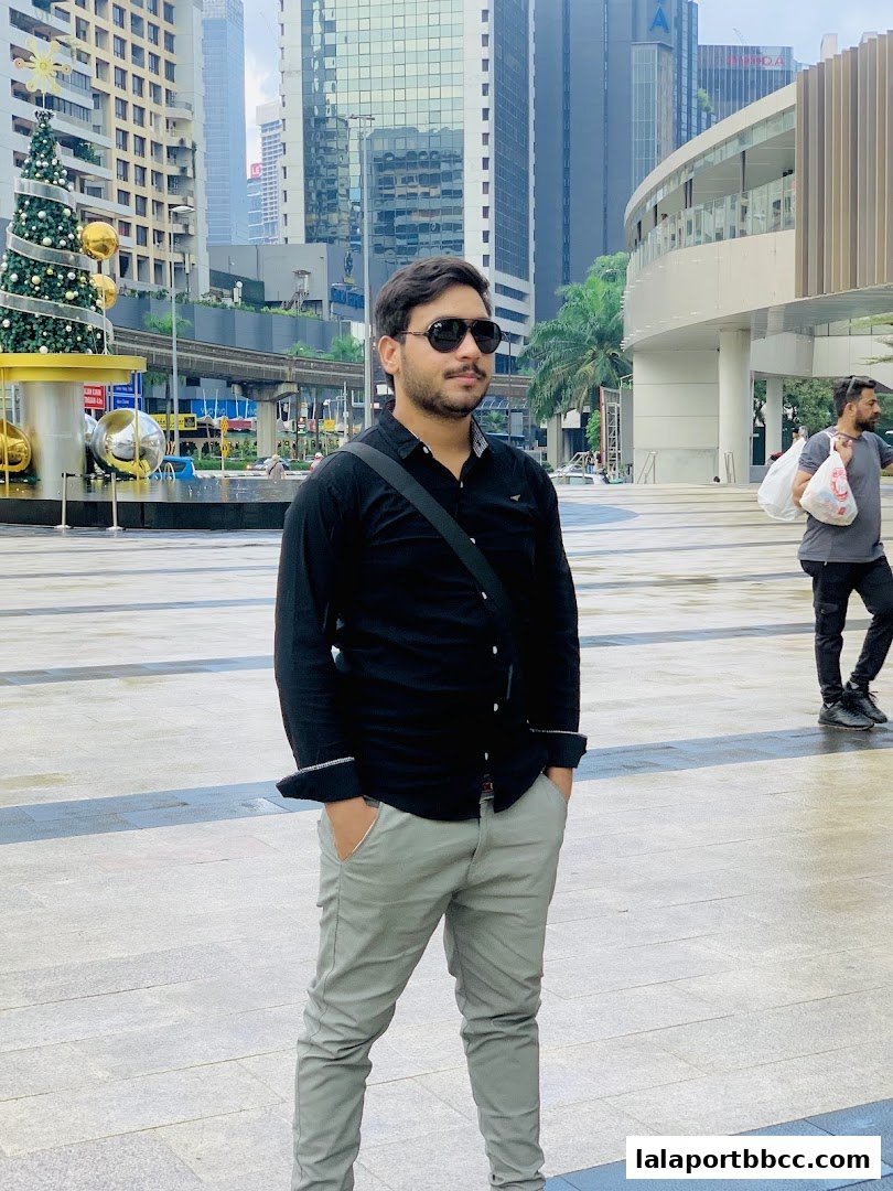 A man poses in front of a modern cityscape with a Christmas tree.