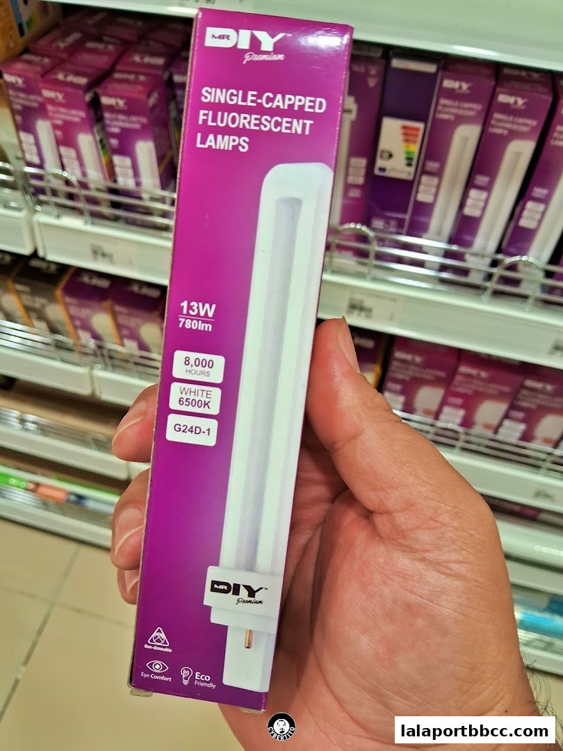 A hand holds a box of MR.DIY Premium single-capped fluorescent lamps in a store aisle.
