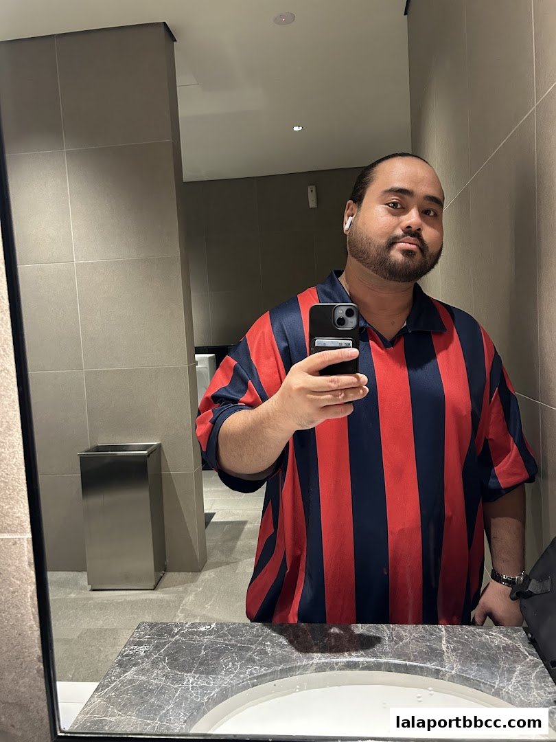 A man in a striped shirt takes a mirror selfie in a modern restroom.