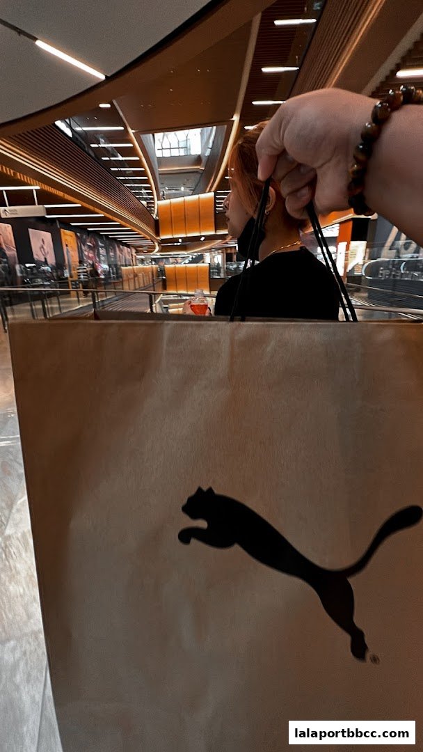 A person carries a PUMA shopping bag in a modern mall with a person in the background.