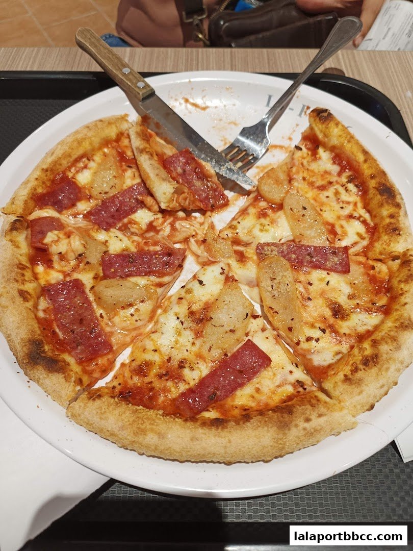 A delicious pizza with salami and pineapple, partially eaten, with cutlery on a white plate.