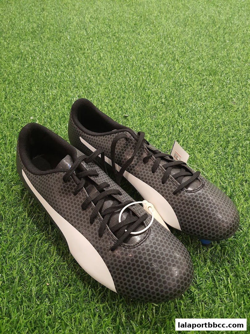 A pair of black Puma soccer cleats with white accents on a green grassy surface.